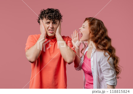 Grumpy woman quarrels on husband or boyfriend On pink. Tired man covers ears Grumpy woman quarrels on husband or boyfriend On pink. Tired man covers ears 118815824