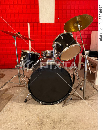Classic black drum set is positioned in a studio with vibrant red soundproof walls. Shiny black drums and bright red background creates a dynamic and energetic music atmosphere. Musical instrument and 118816693