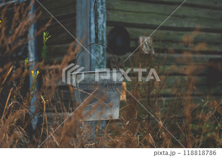 A bucket hangs on a chain against the background of an old, rustic house 118818786