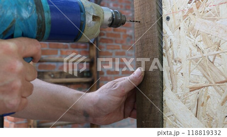 close up of male working hands with drill making hole in wooden material structure, building cage for domestic quails using drilling and fasteners 118819332