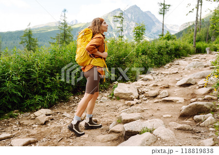 Young female traveler with hiking poles, bright backpack enjoys mountain scenery. Active lifestyle. 118819838