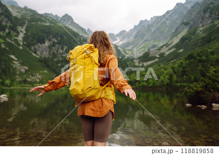 Female traveler with yellow hiking backpack against the backdrop of mountain lake with hiking poles. Female traveler with yellow hiking backpack against the backdrop of mountain lake with hiking poles. 118819858