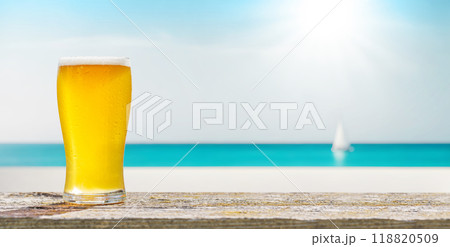 A glass of cold beer sits on a table with a beautiful sea view A glass of cold beer sits on a table with a beautiful sea view 118820509