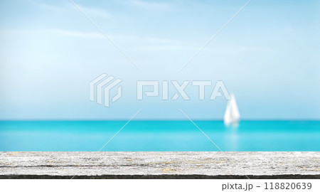 An empty wooden table set in the foreground with a sunny sea horizon and a sailing boat 118820639