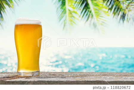 A glass of cold beer sits on a table with a beautiful sea view 118820672