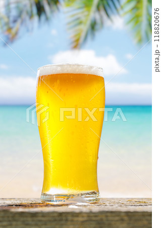 A glass of cold beer sits on a table with a beautiful sea view 118820676