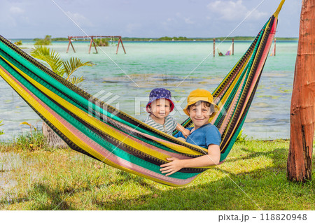 Two boys, a baby and a teenager lying in a hammock against the backdrop of turquoise waters of Bacalar Lake, Mexico. Peaceful tropical travel destination concept 118820948