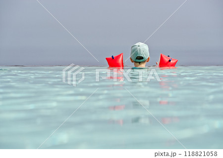 A young child with colorful floaties and a cap looking away from edge of infinity pool A young child with colorful floaties and a cap looking away from edge of infinity pool 118821058