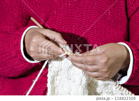 Close-up of woman in red sweater knitting white wool yarn with needles by hand	 118822320