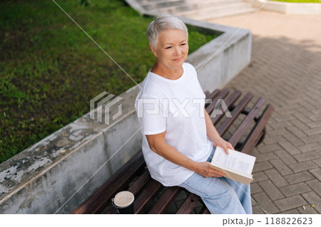 High-angle view of pensive senior woman reading book in city park, thoughtful looking away. Beautiful lady admiring green garden sitting on bench in summer day, resting outdoors alone. High-angle view of pensive senior woman reading book in city park, thoughtful looking away. Beautiful lady admiring green garden sitting on bench in summer day, resting outdoors alone. 118822623