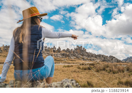 A woman wearing a hat and a blue vest is sitting on a rock in a field, Huayllay. Pasco, Peru. A woman wearing a hat and a blue vest is sitting on a rock in a field, Huayllay. Pasco, Peru. 118823914