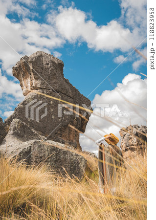 A woman wearing a yellow hat is walking through a field of Huayllay Stone Forest, Peru. 118823958