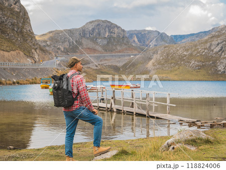 A man wearing a plaid shirt and jeans stands on a bridge overlooking a lagoon seven colors, Road to the Mountain range of the Viuda, Canta. Peru. 118824006