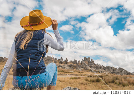 A woman wearing a yellow hat is looking at a car driving down a road, traveling through the peruvian andes 118824018