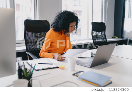 Deep in thought, an African American business consultant in her 30s reviews complex data on her laptop in a bright Deep in thought, an African American business consultant in her 30s reviews complex data on her laptop in a bright 118824500