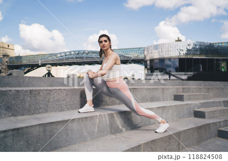 Fitness enthusiast stretches on city stairs, bridge and modern building in backdrop, poised for urban wellness activity 118824508