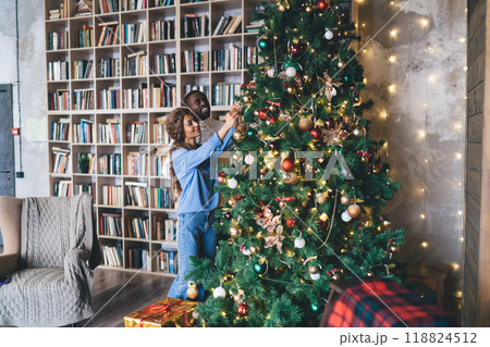 African American man and Caucasian woman in casual attire decorating a Christmas tree African American man and Caucasian woman in casual attire decorating a Christmas tree 118824512