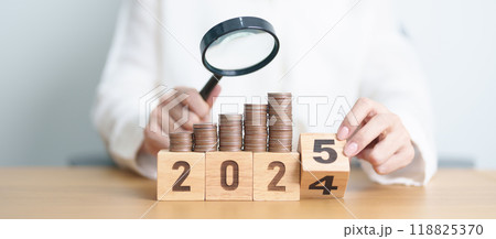 2024 end year to Happy New Year 2025 with  coins money stack growing with magnifier glass. Money saving, Inflation, tax, cash flow, Job search, hiring and research development concepts 118825370