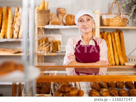 Portrait of elderly woman baker standing behind display case with fresh croissants. Offering to buy fresh baked goods Portrait of elderly woman baker standing behind display case with fresh croissants. Offering to buy fresh baked goods 118827147