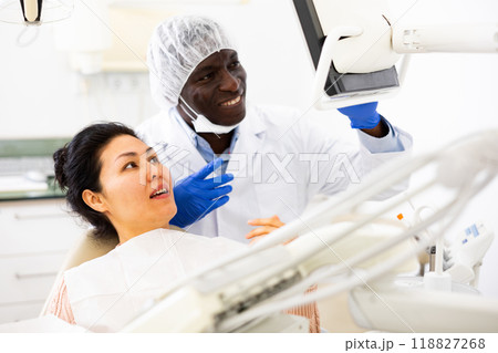 Positive dentist discussing teeth x-ray and treatment procedures with female patient 118827268