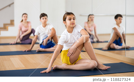 Girl practicing Matsyendrasana during family yoga training at gym Girl practicing Matsyendrasana during family yoga training at gym 118827324