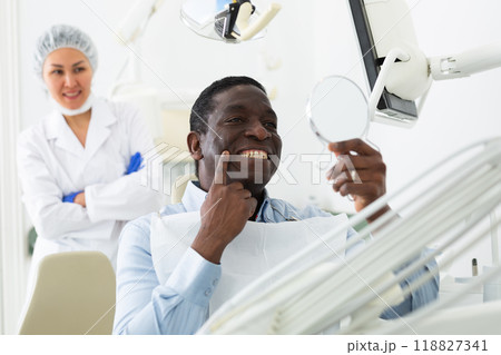 Man looking in mirror to evaluate results of dental restoration procedure 118827341