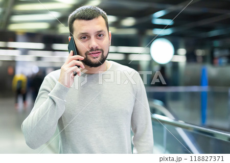 Male passenger in casual clothing talking on his mobile phone next to the subway escalator Male passenger in casual clothing talking on his mobile phone next to the subway escalator 118827371