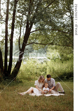 A family of three, a man, a woman and a child, are sitting on a picnic. 118829482