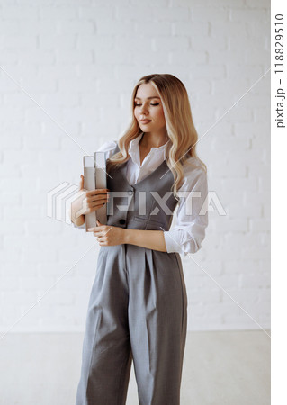 Blonde in a gray suit and white shirt holding a book standing on a white background. 118829510