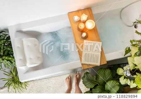 A woman stands in front of a bathtub filled with white foam. The concept of relaxation, self-love A woman stands in front of a bathtub filled with white foam. The concept of relaxation, self-love 118829894