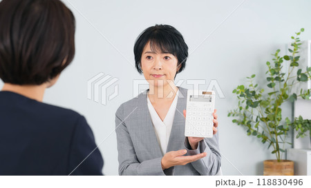 オフィスで電卓を見せて会話する二人の女性ビジネスパーソン オフィスで電卓を見せて会話する二人の女性ビジネスパーソン 118830496