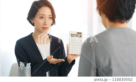 オフィスで電卓を見せて価格交渉する二人の女性ビジネスパーソン 118830502