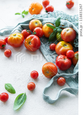 Freshly harvested tomatoes and basil arranged in a reusable net bag on a light kitchen countertop, perfect for cooking or salads Freshly harvested tomatoes and basil arranged in a reusable net bag on a light kitchen countertop, perfect for cooking or salads 118831267