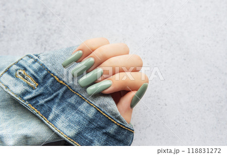 A hand with long green nails resting on a denim sleeve against a textured background A hand with long green nails resting on a denim sleeve against a textured background 118831272