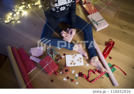 Close up on woman wrapping Christmas presents, sitting on the floor by Christmas tree. Preparing for Christmas Eve. Close up on woman wrapping Christmas presents, sitting on the floor by Christmas tree. Preparing for Christmas Eve. 118832916