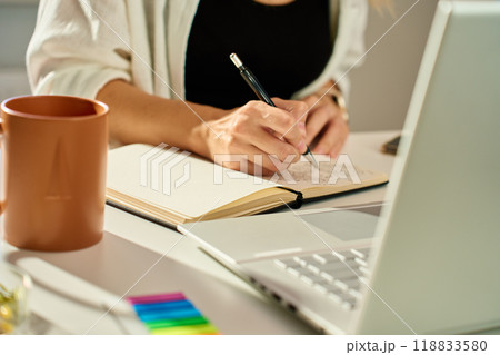 Person is sketching in notebook while working remotely at desk with laptop. Freelance work at home office. Graphic designer drawing sketch 118833580