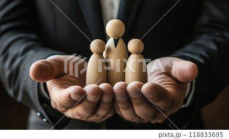 Businessman holding wooden family figures symbolizing protection and care in workplace setting 118833695