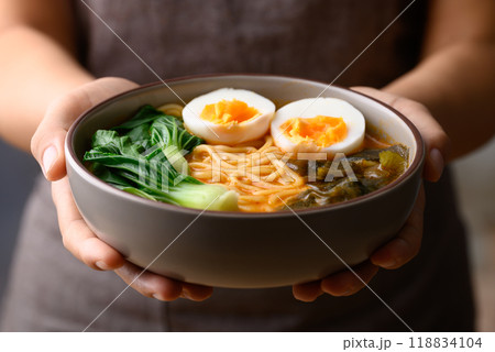 Spicy noodles soup with egg, seaweed and bok choy in bowl holding by hand, Asian noodles style 118834104