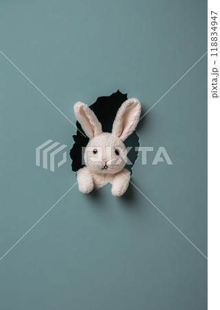 A cute rabbit peeking through a torn blue wall, showcasing a playful and imaginative scene 118834947