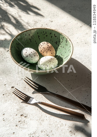 Decorative speckled eggs in a green bowl with blossoming branches on a table setting 118834949