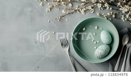 Decorative Easter eggs in a bowl surrounded by blossoms and utensils on a soft grey surface 118834978