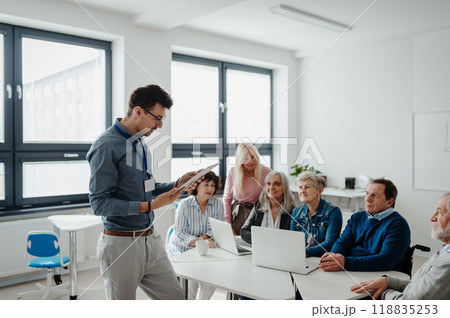 Teacher explaining senior students how to work with laptop and internet. Elderly people attending computer and technology education class. Digital literacy. 118835253