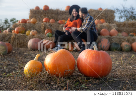 Couple sitting on hay bales in a pumpkin patch Couple sitting on hay bales in a pumpkin patch 118835572
