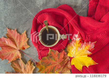 Autumn still life: Cup of hot coffee wrapped in a red knitted scarf and autumn leaves on a dark background 118836179