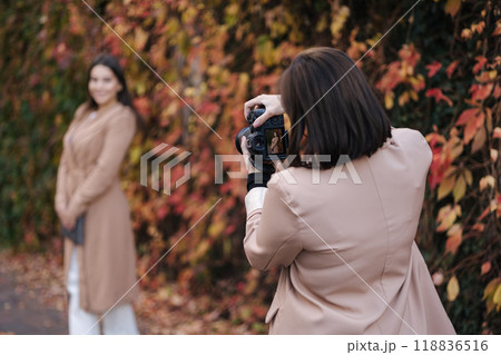 Back view of female photographer makes a photo for beautiful woman. Autumn mood 118836516