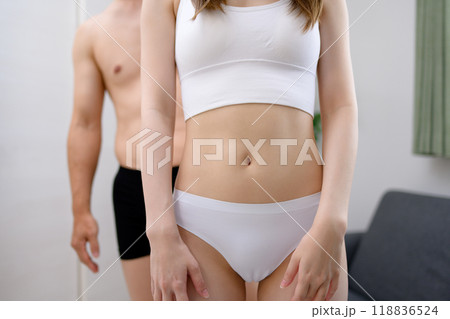 下着姿の女性の後ろに立つ男性　男女のカップル　夫婦　妊活　協力　室内リビング 118836524