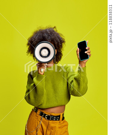 Woman with megaphone in one hand and smartphone in other, ready for social media against green studio background. Woman with megaphone in one hand and smartphone in other, ready for social media against green studio background. 118838311