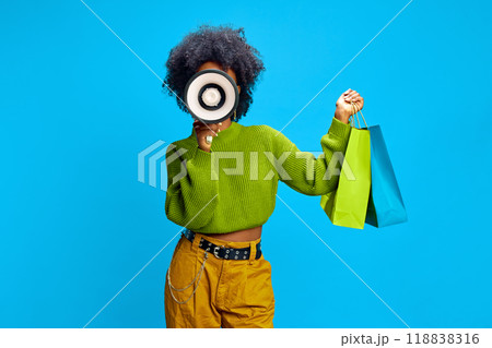 Fashionable woman in green sweater holds megaphone in one hand and shopping bags in other, signaling exciting promotion. Fashionable woman in green sweater holds megaphone in one hand and shopping bags in other, signaling exciting promotion. 118838316