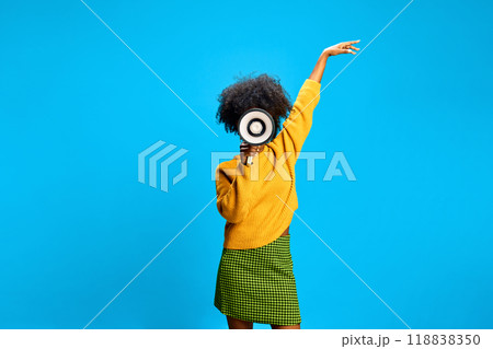Woman shouting to megaphone, pointing to sky, inspiring confidence against bright blue studio background. 118838350