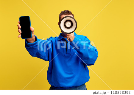Man holds smartphone and megaphone, ready to announce latest mobile updates or services against yellow background. Man holds smartphone and megaphone, ready to announce latest mobile updates or services against yellow background. 118838392